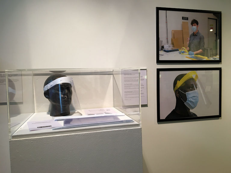 A visor on display in a case next to two framed images of the item being made and worn.