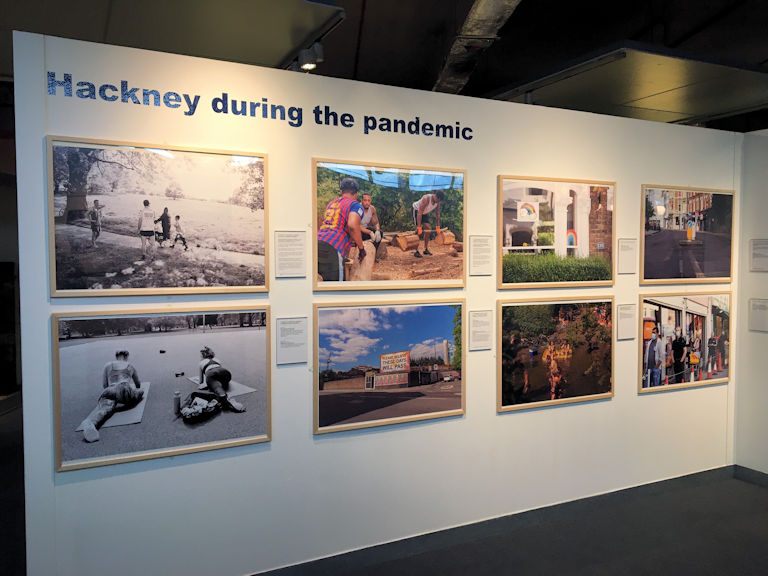 Shot of a photography display. 8 large framed photographs are on a wall under the heading 'Hackney During the Pandemic'