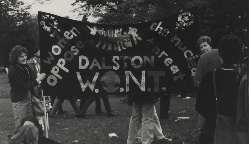 Black and white photograph of women in a park holding a banner reading 'Women Oppose the Nuclear Threat Dalston W.O.N.T'