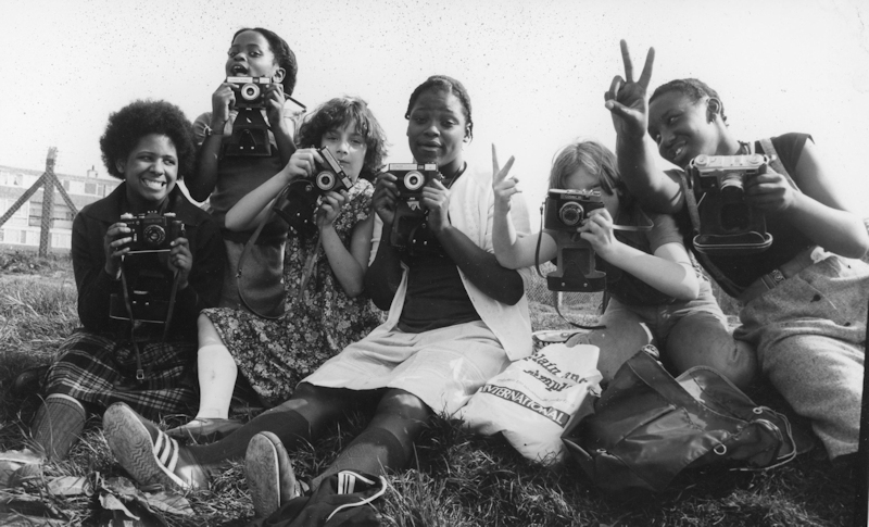 Black and white photograph of six teenage girls, members of the Hackney Girls Project, posing while holding cameras