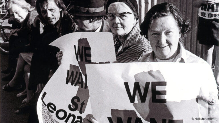 A row of campaigners, with two women looking at the camera and holding campaign posters.