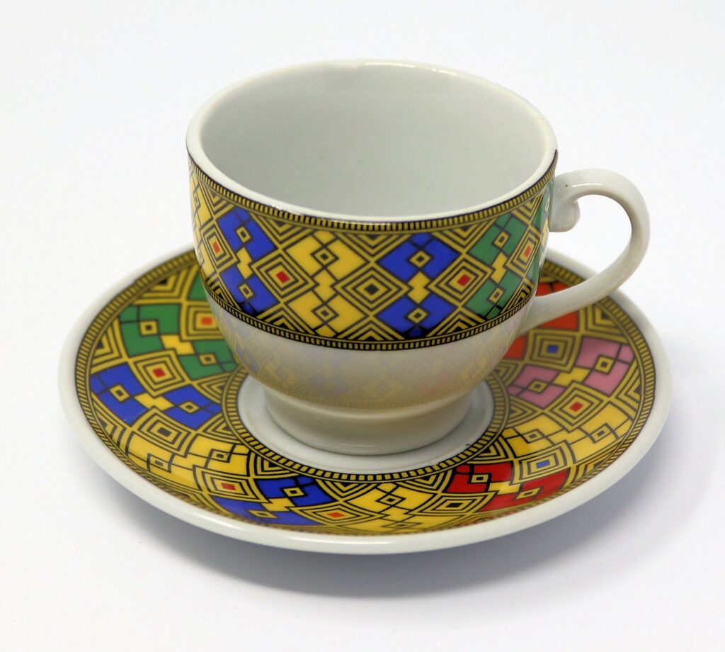 Coffee cup and saucer with yellow, blue, red, green and gold printed designs