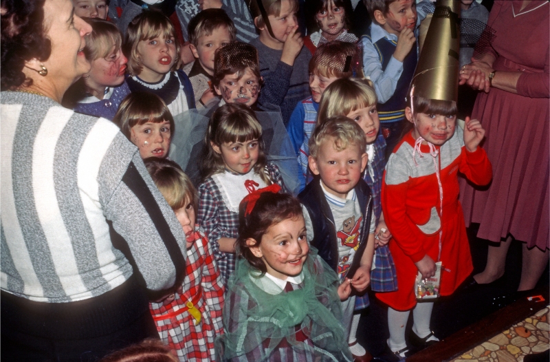 A colour photograph of a group of small children at a Christmas party, some wearing face paints and one wearing a party hat.