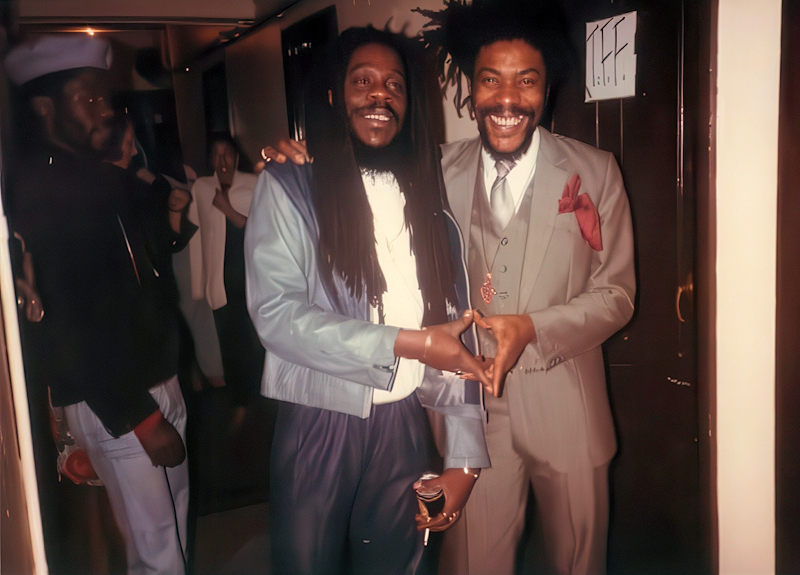 Two men posing for the camera. They have each joined one of their hands with the others to make a heart symbol.